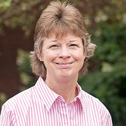 A photo of Susan standing outside in front of a tree smiling at the camera.