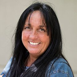 A photo of Shirley standing outside in front of a wall smiling at the camera.