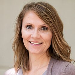 A photo of Rachael standing outside in front of a wall smiling at the camera.