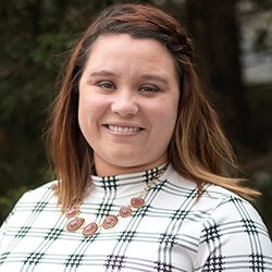 A photo of Emily standing outside in front of a tree smiling at the camera.