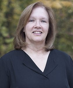 A photo of Sally standing outside in front of a tree smiling at the camera.