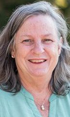 A photo of Mary standing outside in front of a tree smiling at the camera.