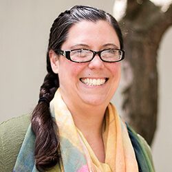 A photo of Kate standing outside in front of a tree smiling at the camera.