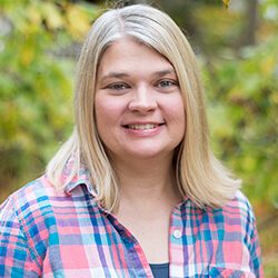 A photo of Tammy standing outside in front of a tree smiling at the camera.