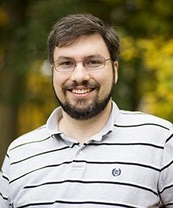 A photo of Jay standing outside in front of a tree smiling at the camera.