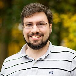 A photo of Jay standing outside in front of a tree smiling at the camera.