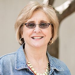 A photo of Pat standing outside in front of a tree smiling at the camera.