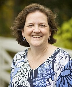 A photo of Mary standing outside in front of a tree smiling at the camera.