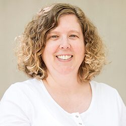 A photo of Mary standing outside in front of a wall smiling at the camera.