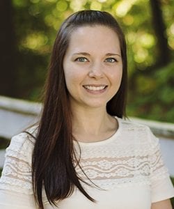 A photo of Kari standing outside in front of a tree smiling at the camera.