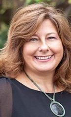 A photo of Darlene standing outside in front of a tree smiling at the camera.