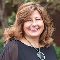 A photo of Darlene standing outside in front of a tree smiling at the camera.