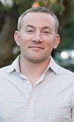 A photo of Aaron standing outside in front of a tree smiling at the camera.