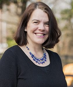 A photo of Joanne standing outside in front of a tree smiling at the camera.