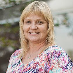 A photo of Suzanne standing outside in front of a tree smiling at the camera.