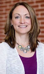 A photo of Hallie standing outside in front of a brick wall smiling at the camera.