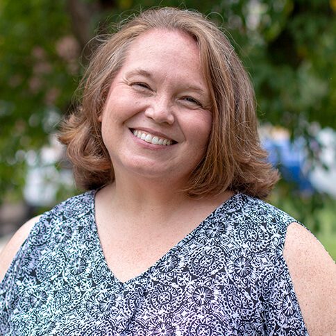 A photo of Jill standing outside in front of a tree smiling at the camera.