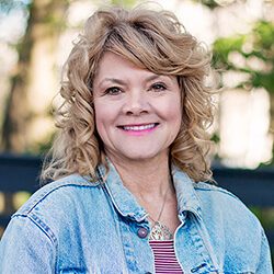 A photo of Cyndi standing outside in front of a tree smiling at the camera.