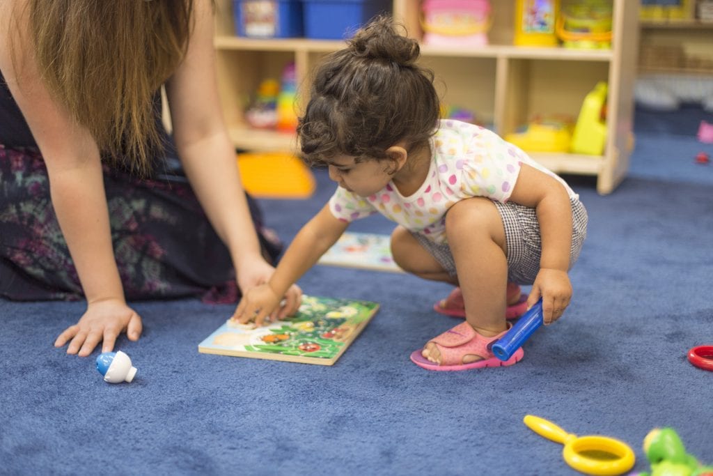 A child is pointing to a picture in a book. Beside her, an adult is ready to turn the page.