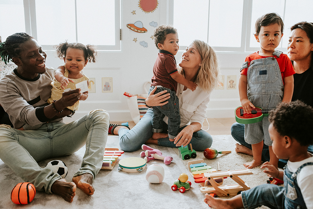 Diverse children playing on the floor of a child care center with three adults with various toys