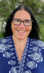 Woman with black hair wearing a blue shirt with white embroidery