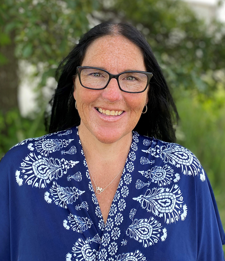 Woman with black hair wearing a blue shirt with white embroidery