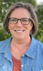 Woman with short light brown hair wearing a orange shirt with a denim jacket