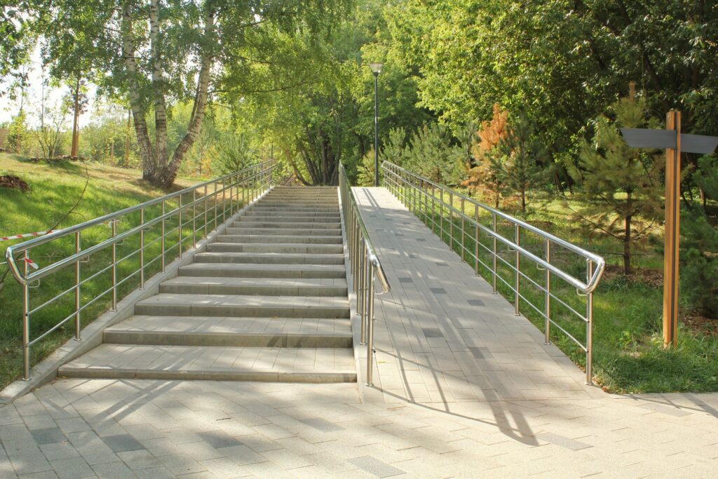 A ramp on the right and a set of stairs on the left, with handrails along the outside and between the two, that leads to the top of a small incline.