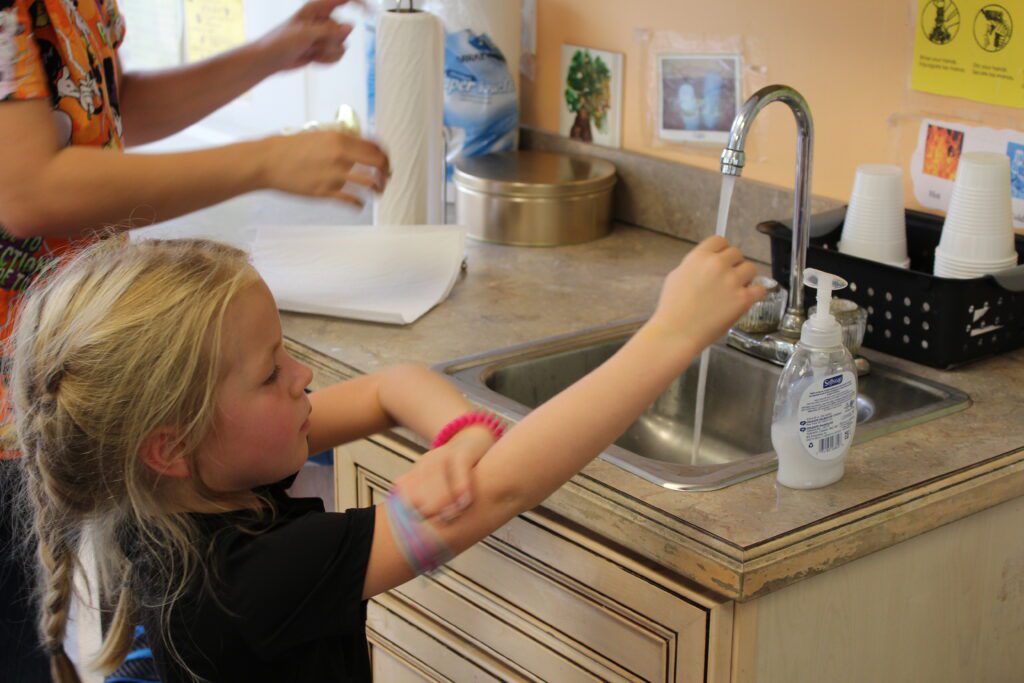 Child at a sink with soap getting ready to wash their hands.