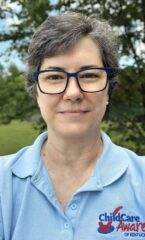 A woman with short dark hair wearing navy rimmed glasses and a light blue polo shirt.